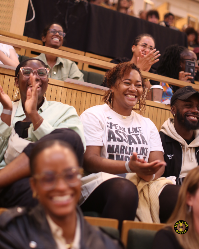 Crowd picture of two rows Black people sitting in a theatre smiling and giving applause.